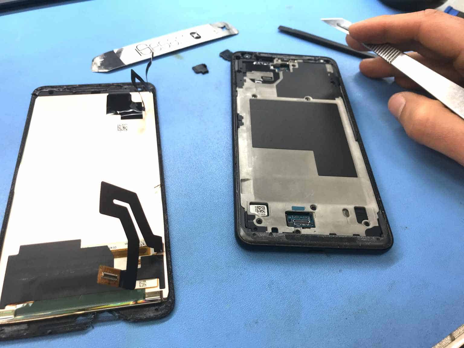 A replacement phone screen assembly lying beside the opened frame it will go into, with its ribbon cables laid out