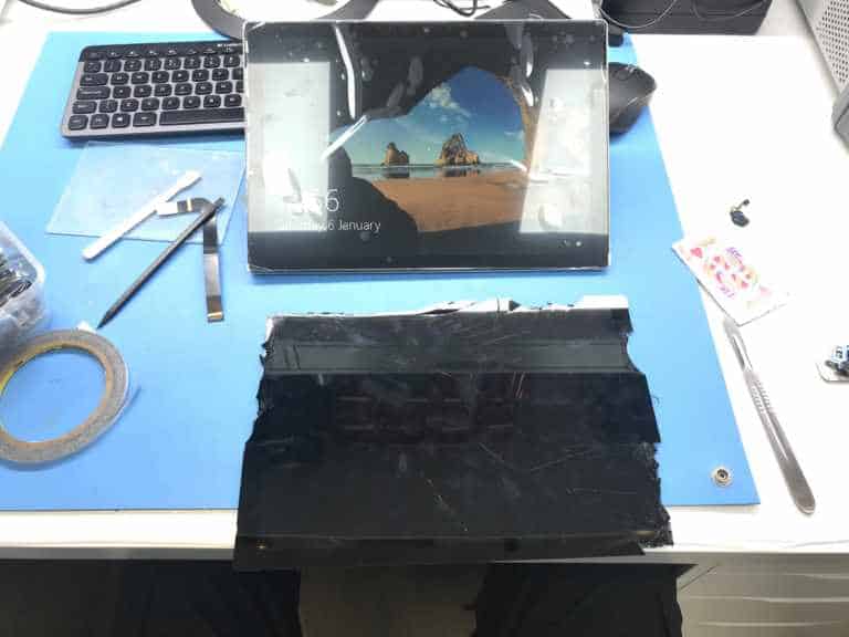 A Surface Pro running on its new screen, with the removed cracked screen lying below it