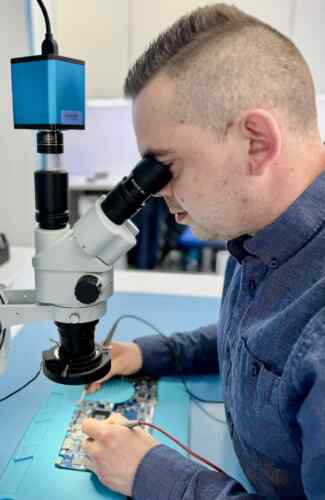 Fixfactor Technician Diagnosing Laptop Motherboard Through Microscope Left Perspective