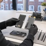 Technician comparing replacement phone display assemblies at a repair bench