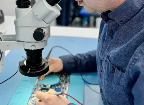 Adam, Fixfactor technician in Wimbledon, testing a motherboard under the microscope with a multimeter probe