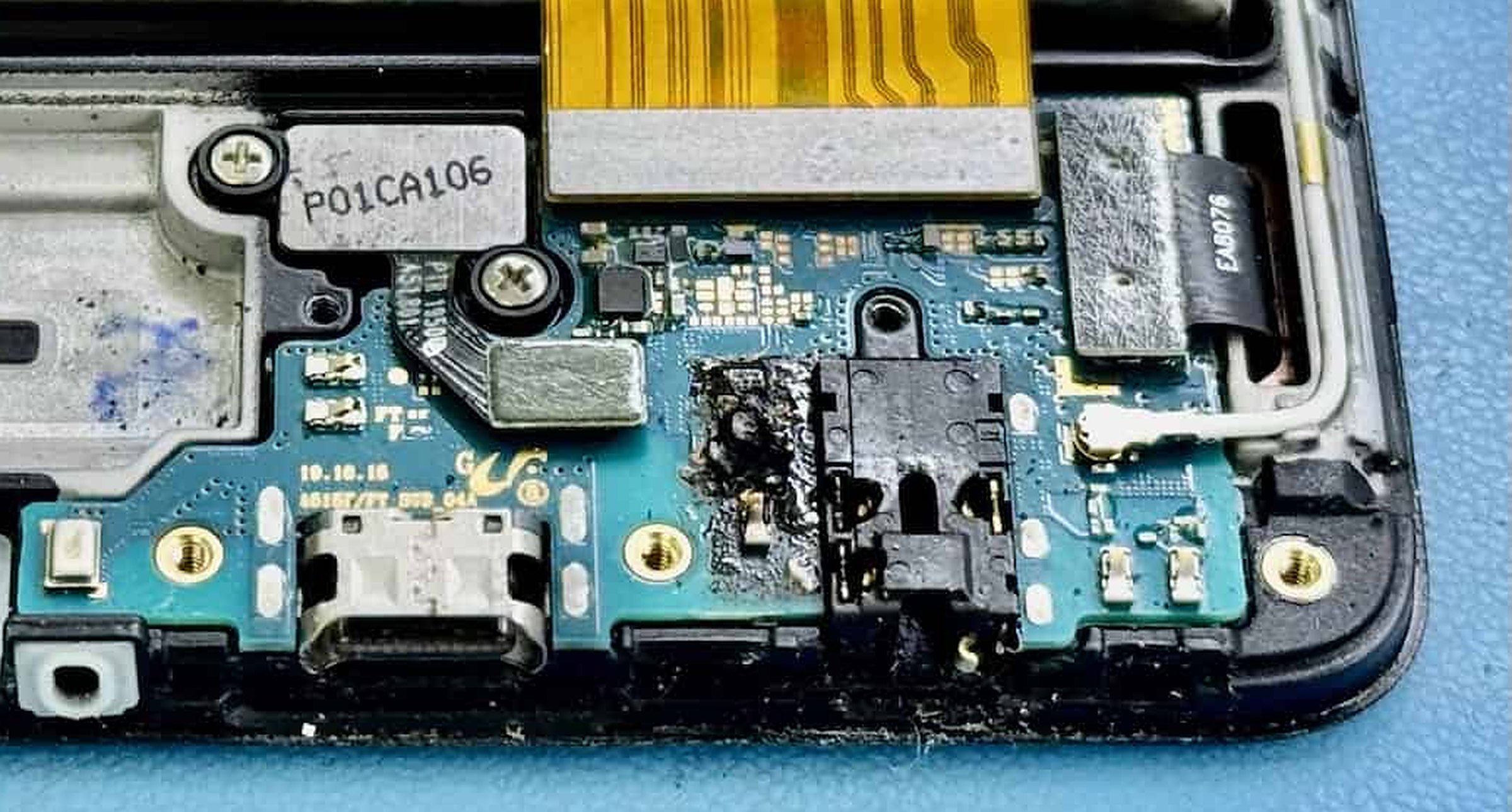 Macro of a corroded phone mainboard: burnt residue around components beside the charging port after liquid damage.