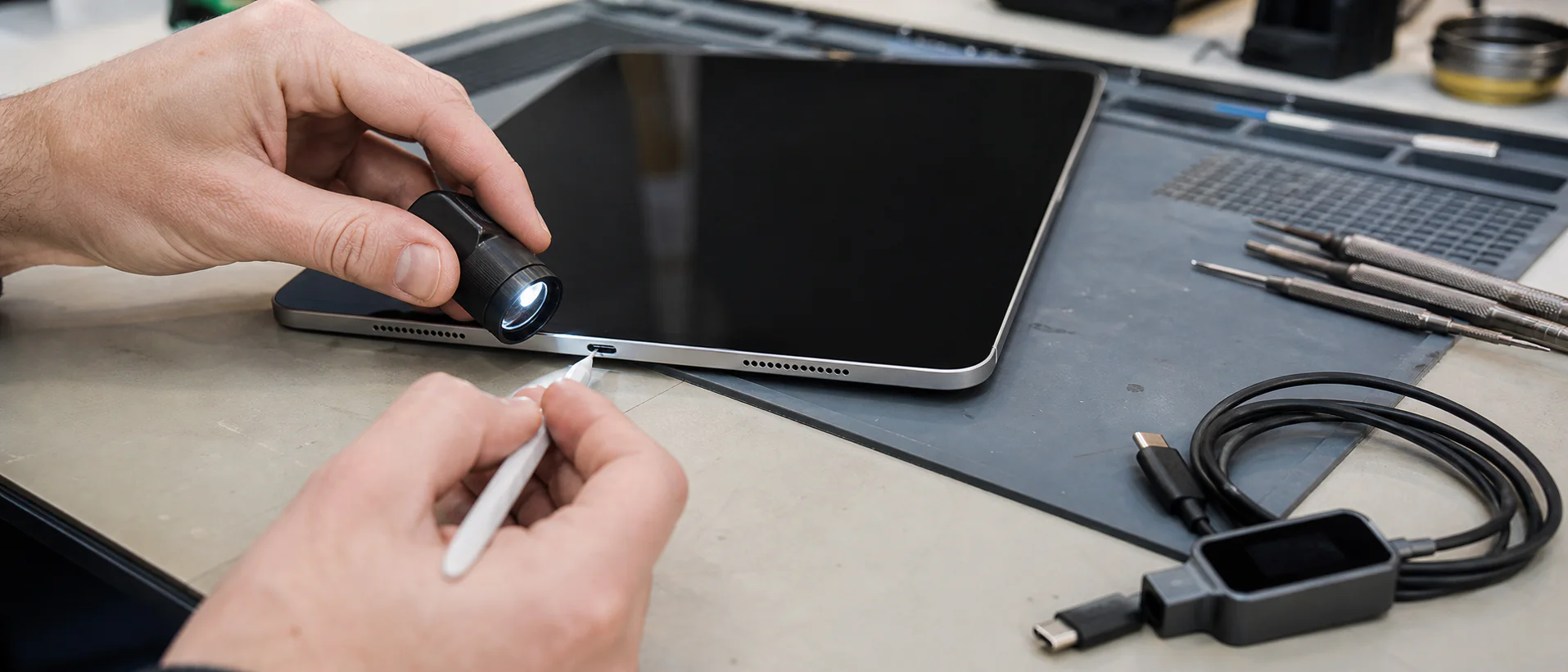 Technician inspecting an iPad USB-C charging port under a work light